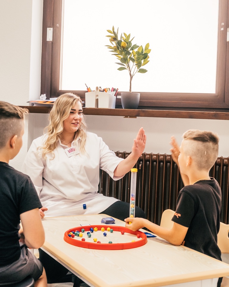 Mareike Grimm gibt einem Jungen am Therapietisch ein High-Five