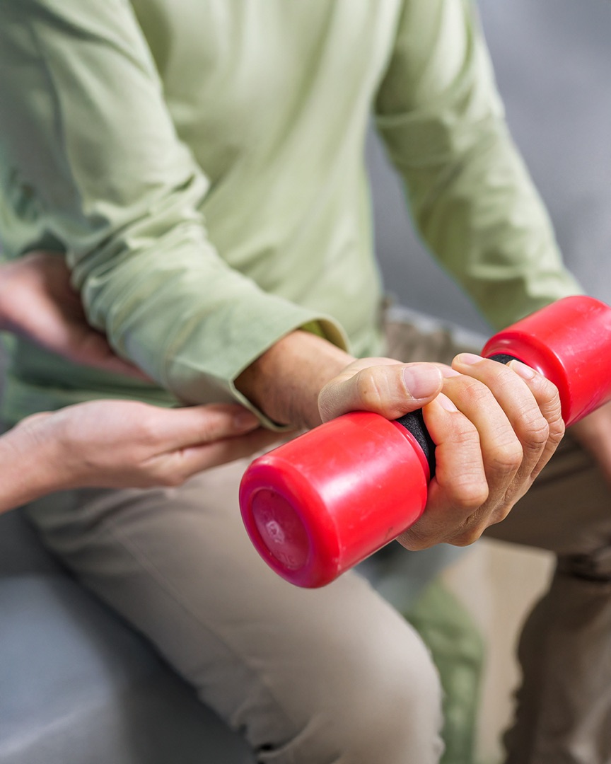 Patient drückt einen roten Handtrainer, angeleitet von der Therapeutin