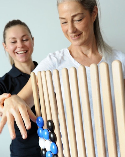 Zwei Therapeutinnen lachen beim Üben mit einer Holzleiter